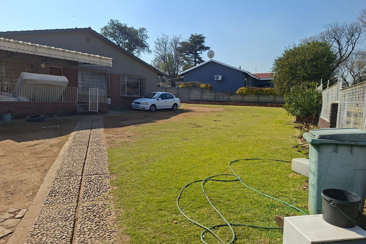 Spacious rear garden featuring a paved walkway, a covered patio area, and perimeter brick boundary walling.