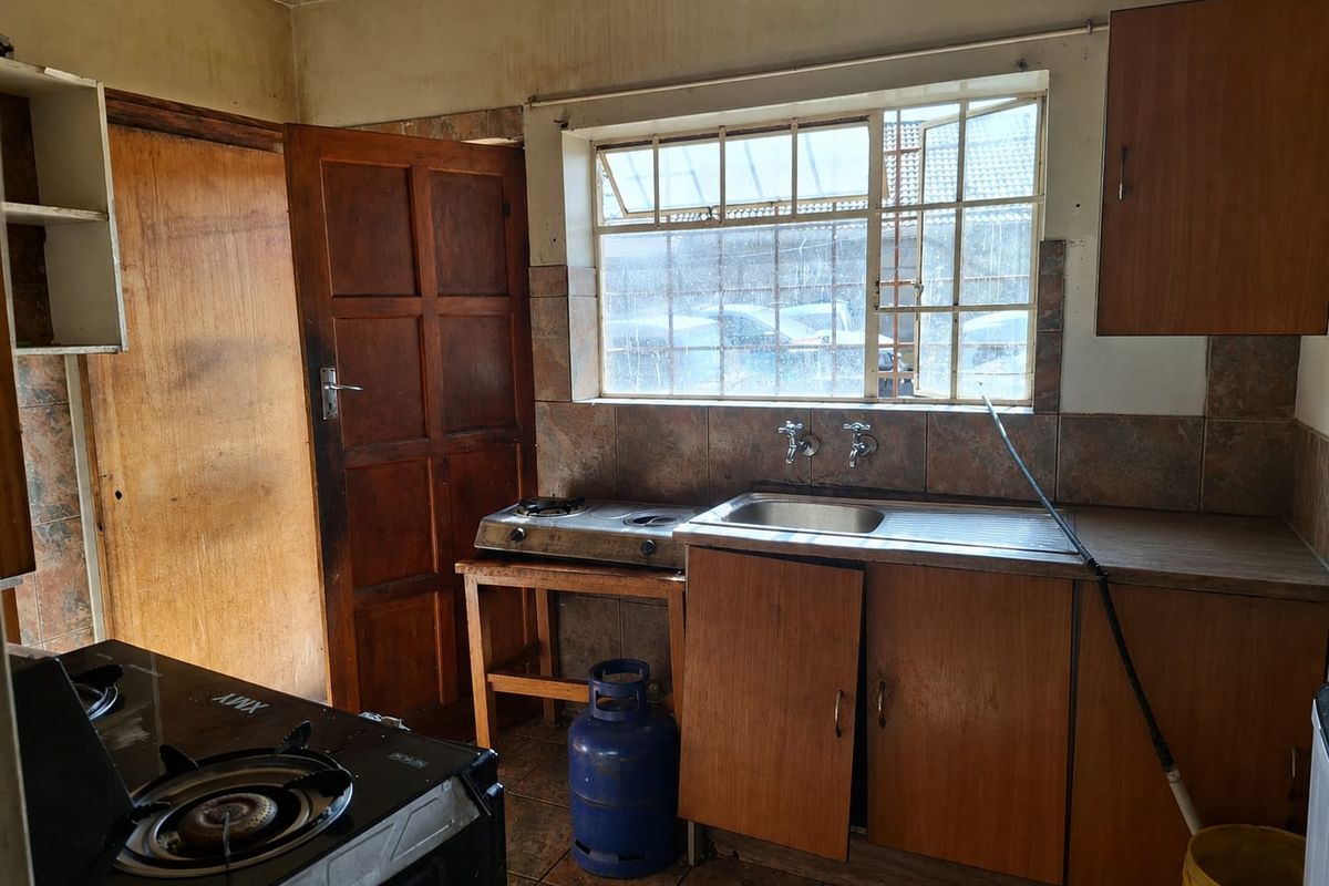 A dated kitchen featuring wooden cabinetry, a stainless steel sink, and tiled splashbacks, requiring significant renovation and cosmetic updates to modernize the space.