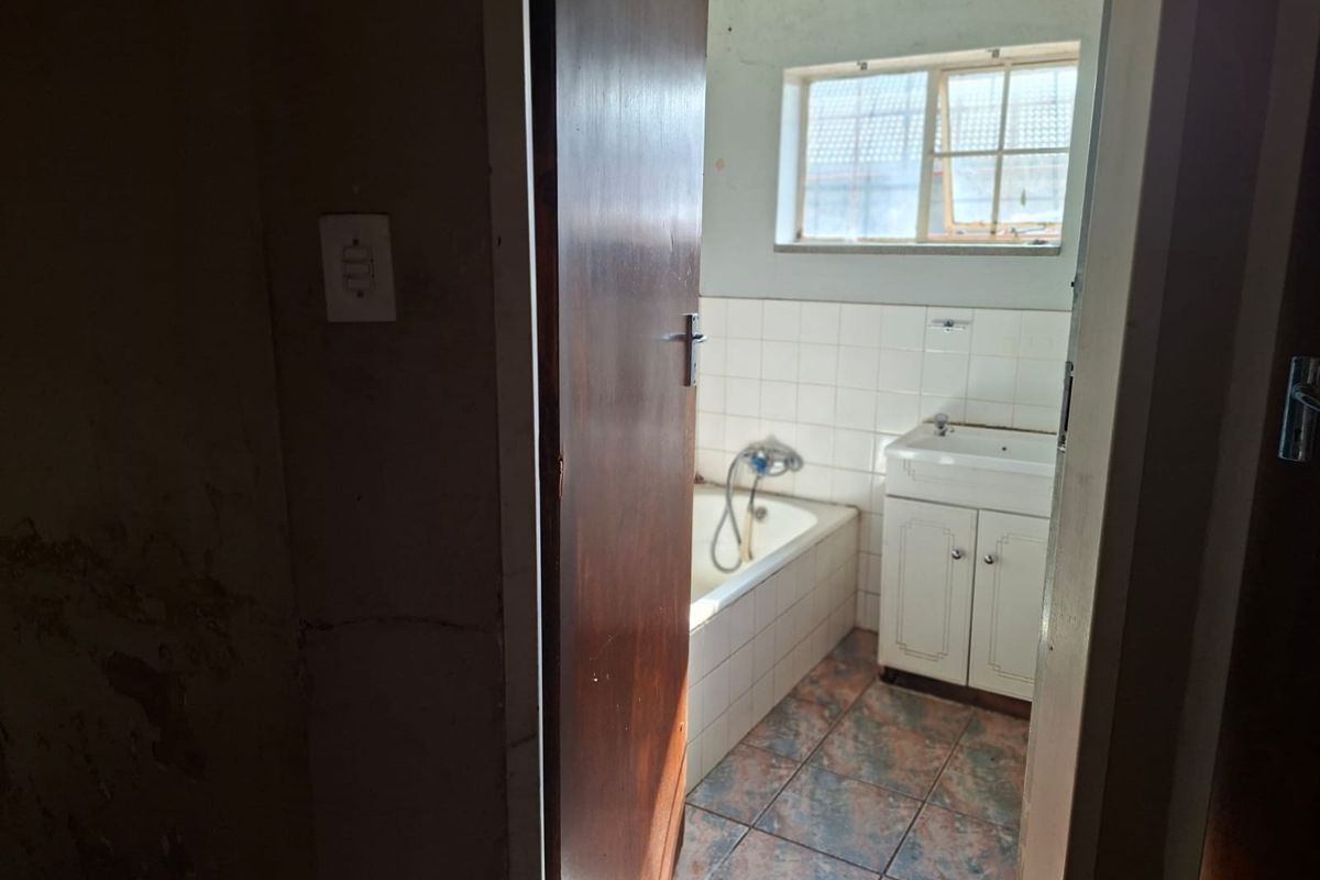 A dated bathroom featuring a built-in vanity and bathtub, requiring renovation to address worn finishes and surface damage.