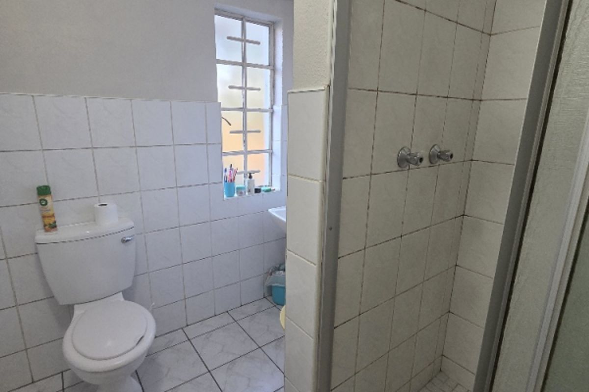 A functional bathroom featuring a shower enclosure, toilet, and tiled finishes throughout, offering a practical layout with natural light from the window.