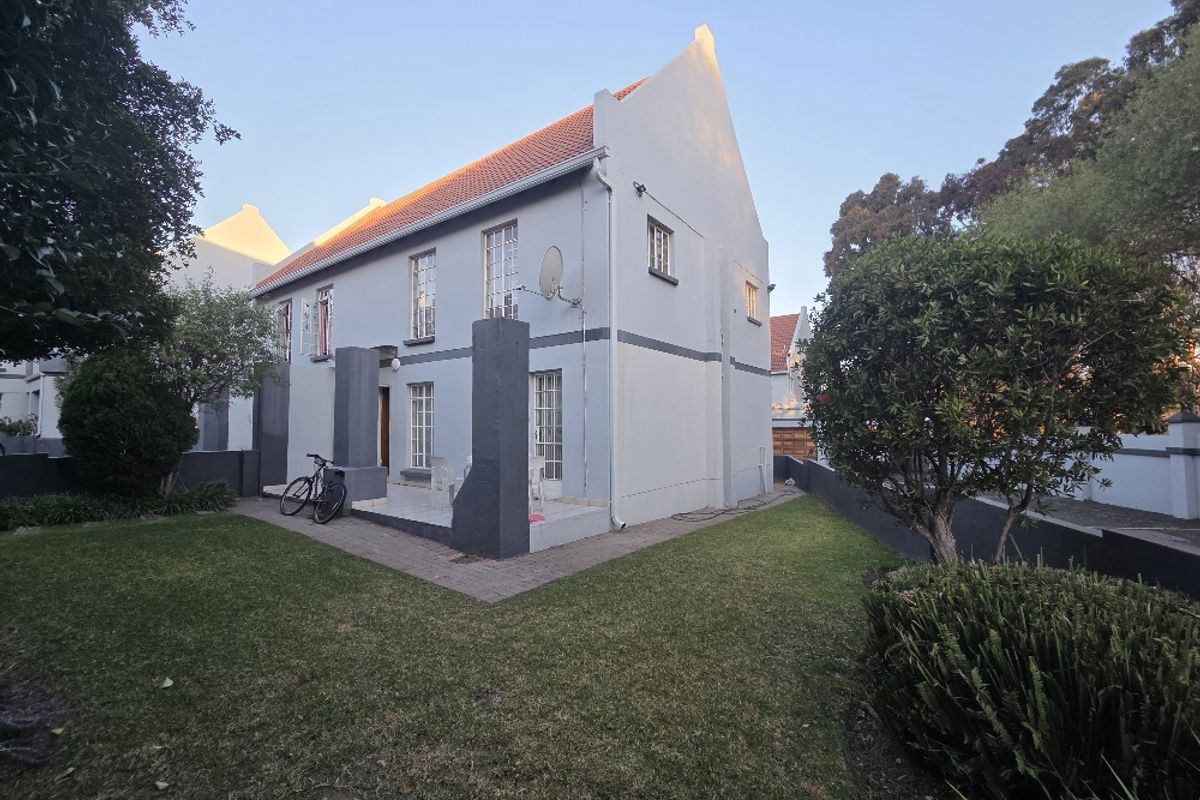 Rear view of a townhouse featuring a gabled roof, paved patio area, and surrounding garden space with boundary walls.