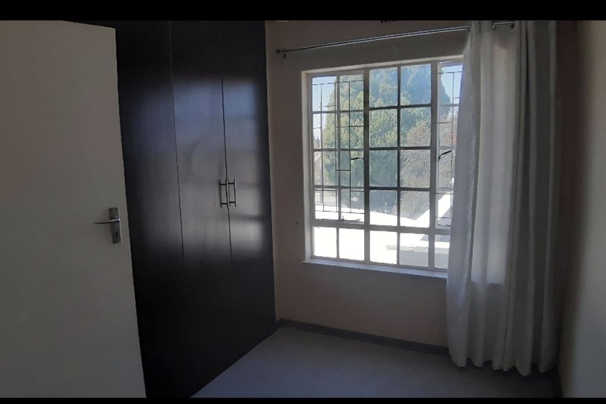 A vacant bedroom featuring a dark built-in wardrobe and a window fitted with security bars.