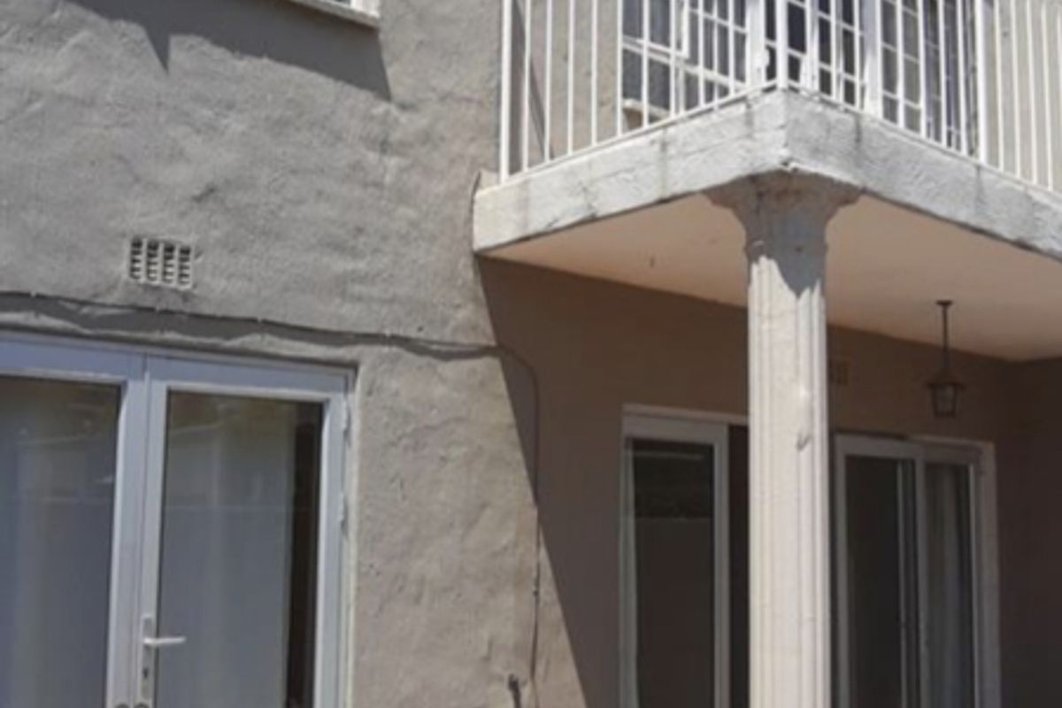 Rear exterior view of the townhouse featuring a tiled patio, a balcony with a support column, and multiple glass sliding doors and casement windows.