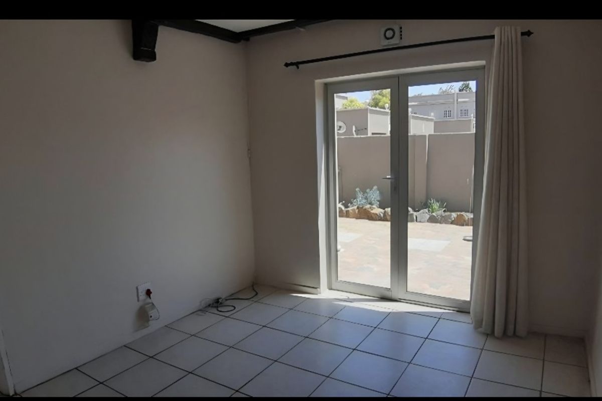 An empty living room featuring tiled flooring, exposed ceiling beams, and double glass doors providing direct access to the rear patio area.