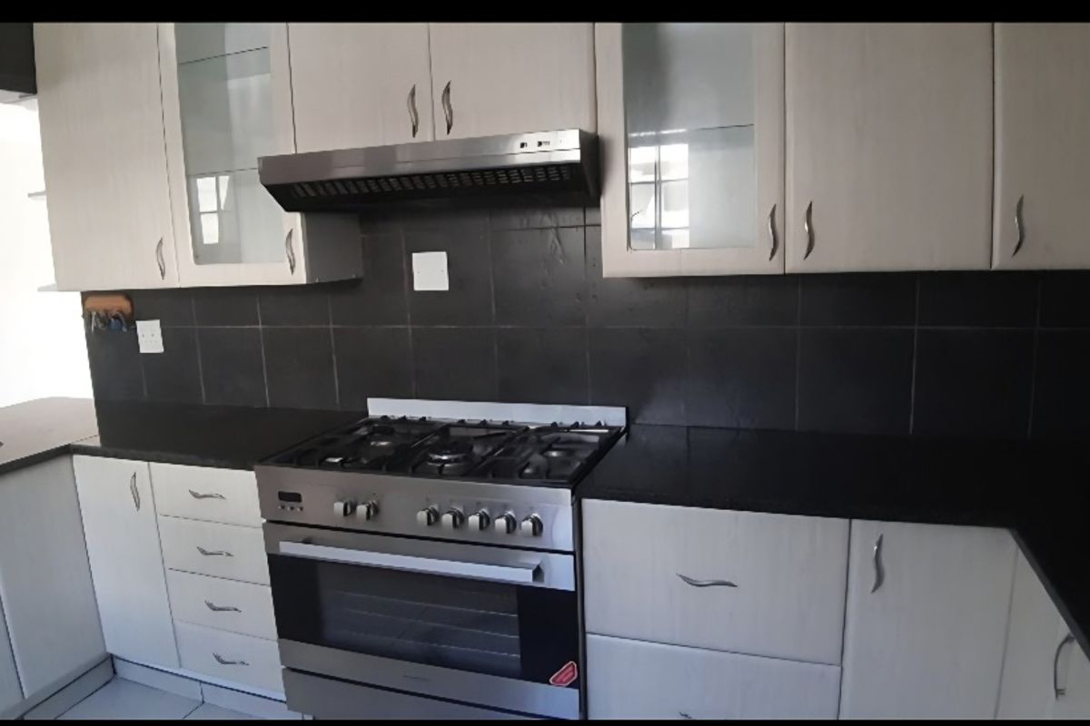 A functional kitchen featuring light-toned cabinetry, dark stone countertops, a gas stove with an integrated extractor fan, and a dark tiled backsplash.