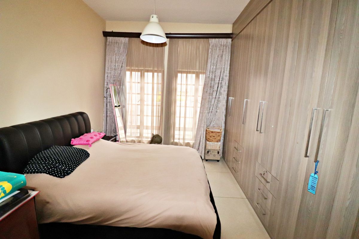 A well-maintained bedroom featuring extensive built-in wooden cupboards, tiled flooring, and large windows with curtain tracks, providing ample storage and natural light.
