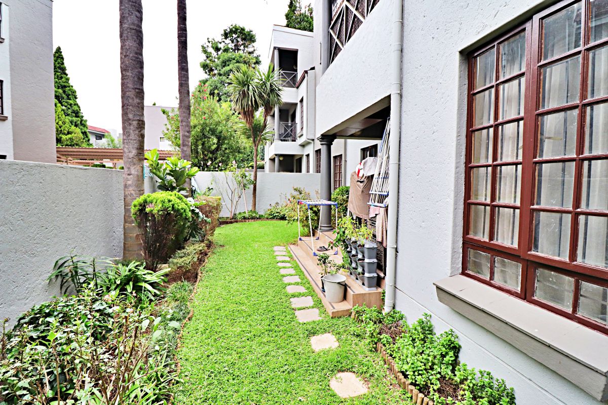 A private rear garden area featuring a manicured lawn, stone stepping path, and established perimeter landscaping adjacent to the apartment building.