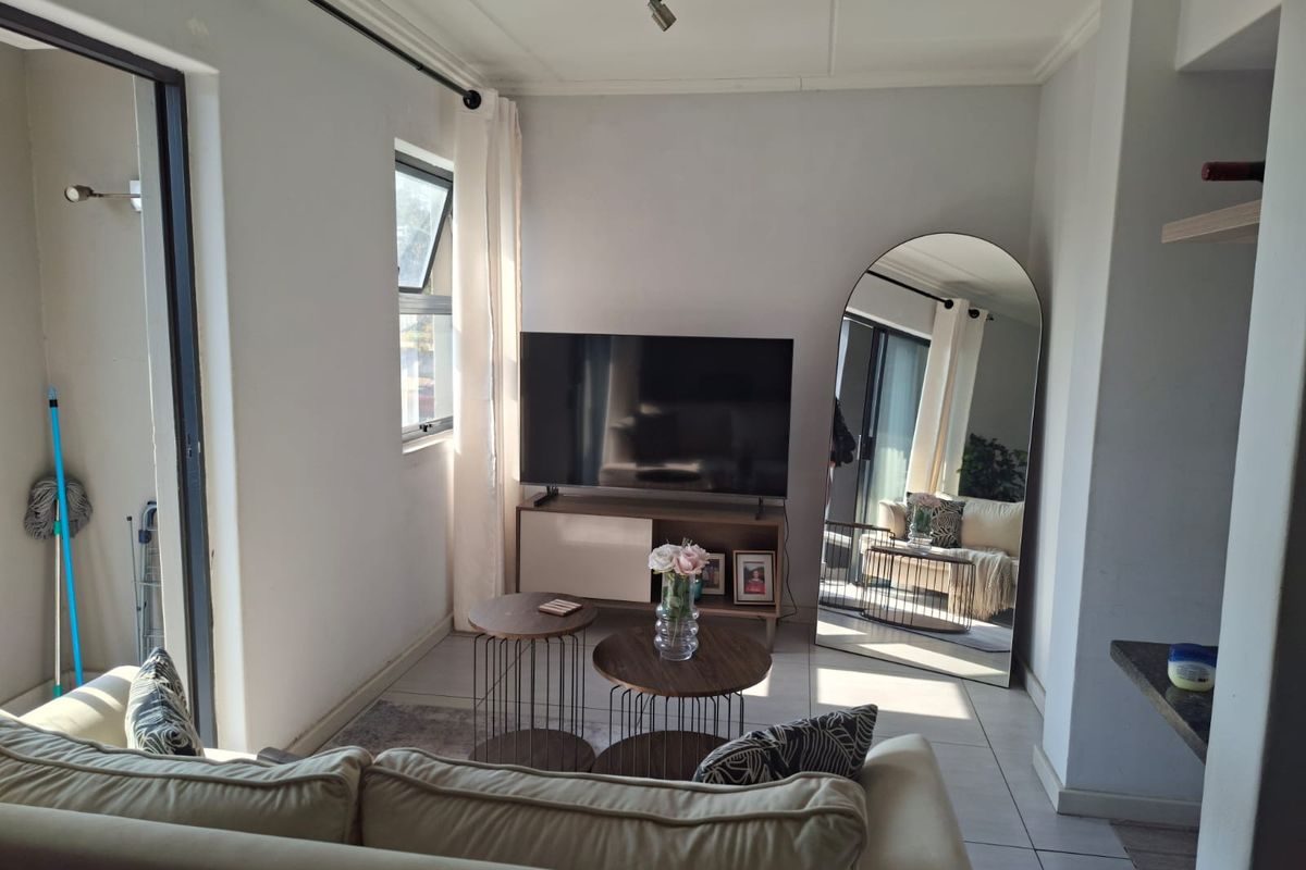 A compact living room featuring tiled flooring, neutral walls, and a sliding door providing access to an adjoining balcony area.