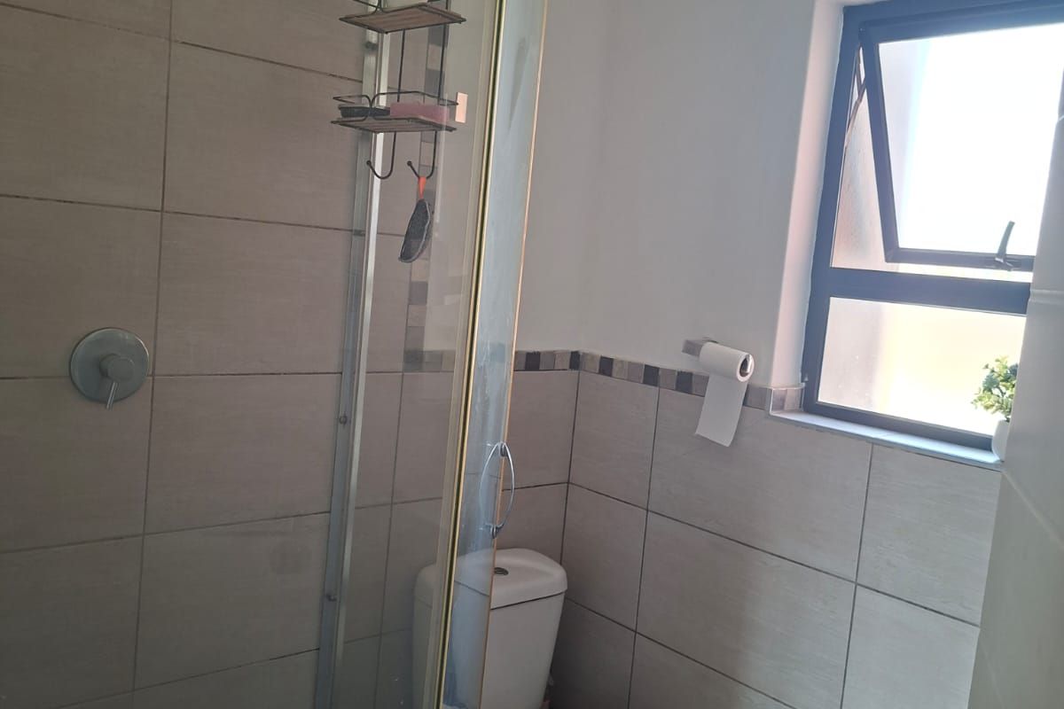 A functional bathroom featuring a glass-enclosed shower with a rain shower head, a toilet, and neutral wall tiling.