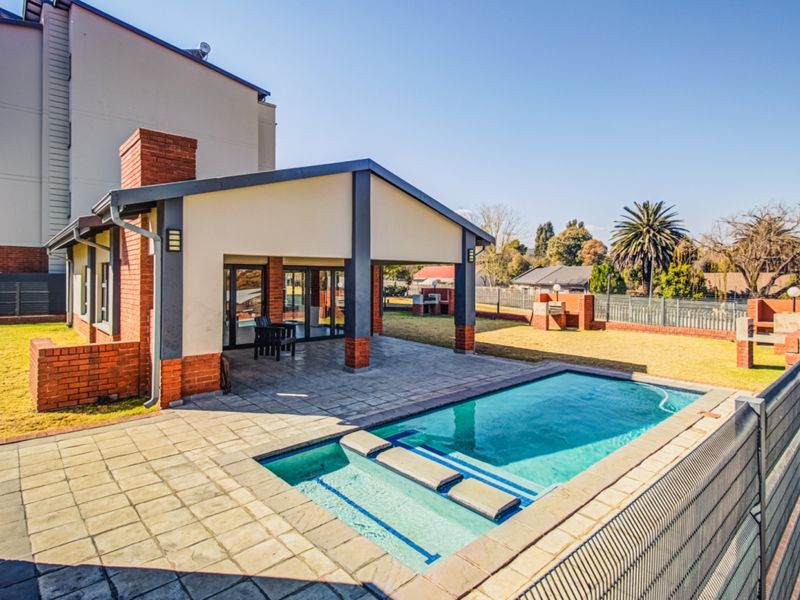 Outdoor entertainment area featuring a swimming pool, paved deck, and a covered patio with a built-in braai, perfect for relaxed outdoor living.
