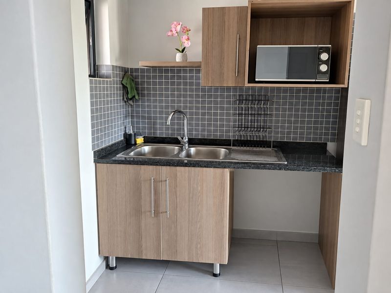 Compact scullery area featuring modern wood-look cabinetry, granite countertops, a double bowl stainless steel sink, and a tiled backsplash.