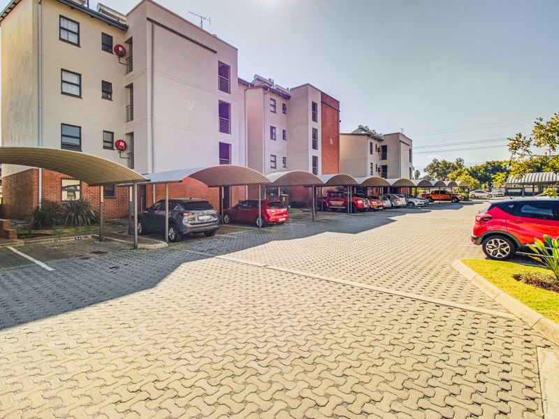 Exterior view of a multi-story apartment complex featuring paved parking areas with covered carports and well-maintained building facades.