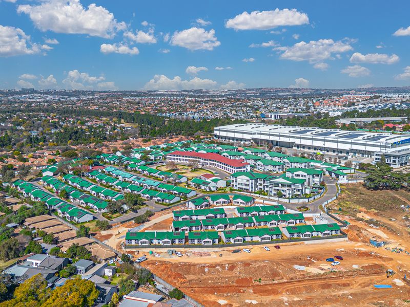 An aerial view of a residential apartment complex featuring uniform green roofs, paved access roads, and surrounding suburban infrastructure.