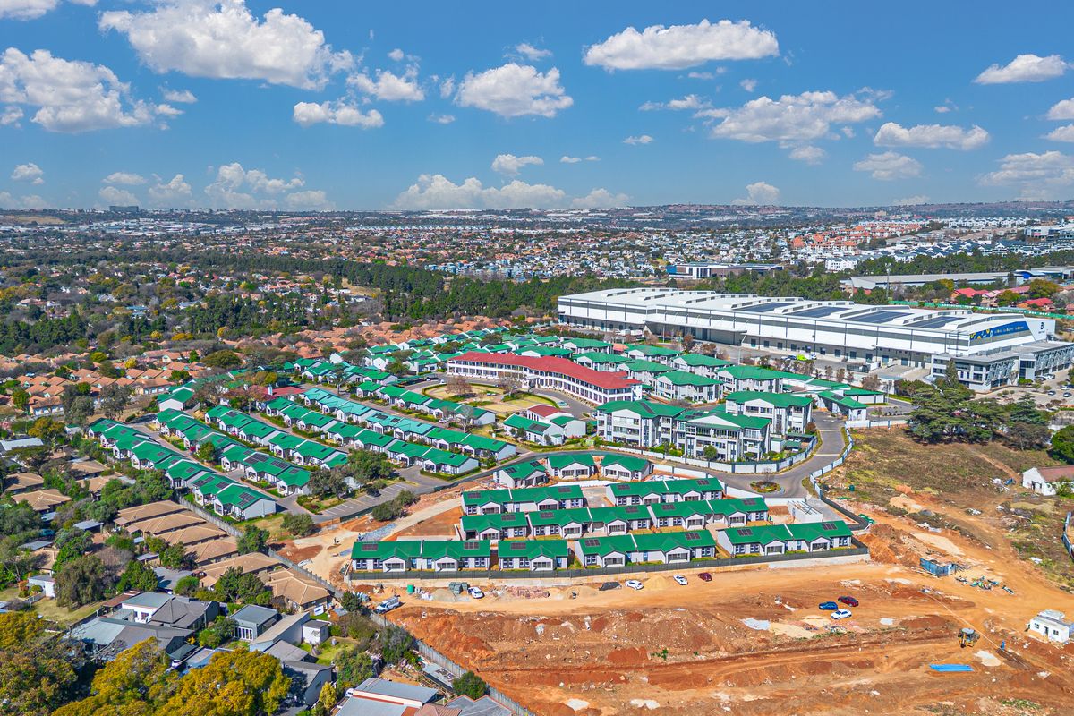 An aerial view of a residential apartment complex featuring uniform green roofs, paved access roads, and surrounding suburban infrastructure.