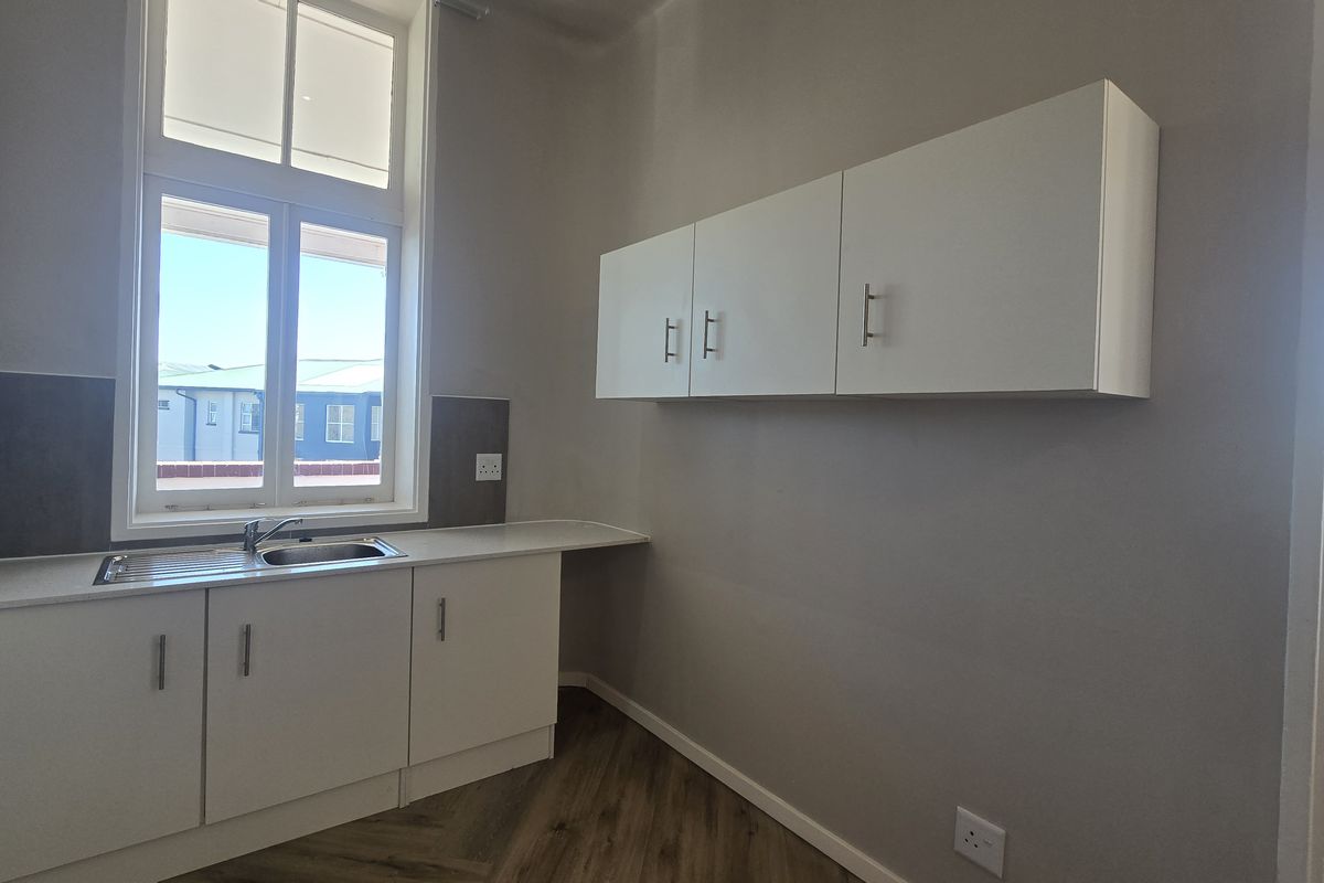 A clean, modern kitchen area featuring white built-in cabinetry, a stainless steel sink, and durable laminate flooring with ample natural light.