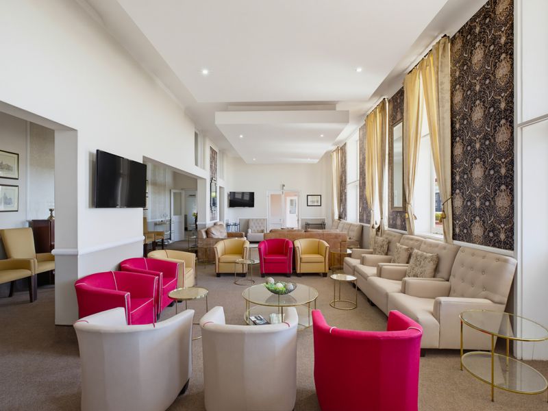 Spacious living area featuring high ceilings, recessed lighting, large windows with drapes, and a decorative patterned feature wall.