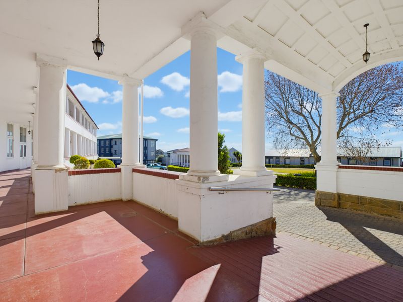 A spacious covered patio featuring classical columns, a vaulted ceiling, and a paved driveway view, offering a grand entrance to the property.
