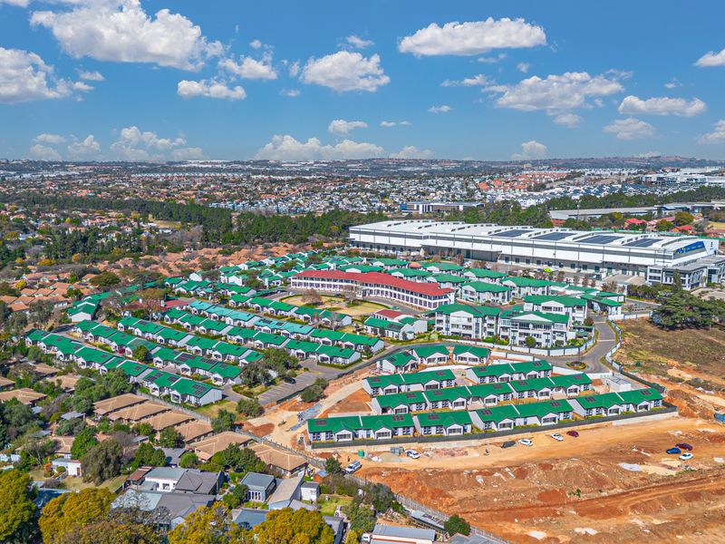 Aerial view of a residential apartment complex featuring uniform green roofs, paved roads, and proximity to industrial infrastructure.