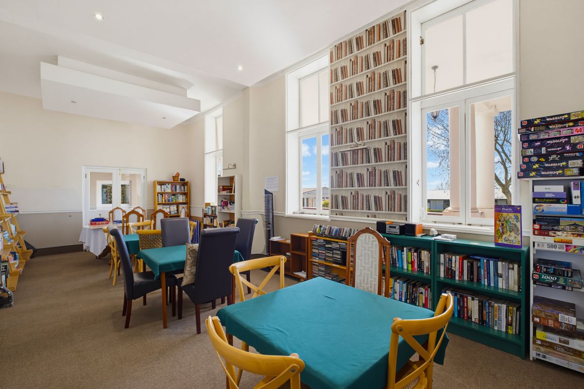 A spacious living area featuring high ceilings, large windows providing natural light, and built-in shelving units.