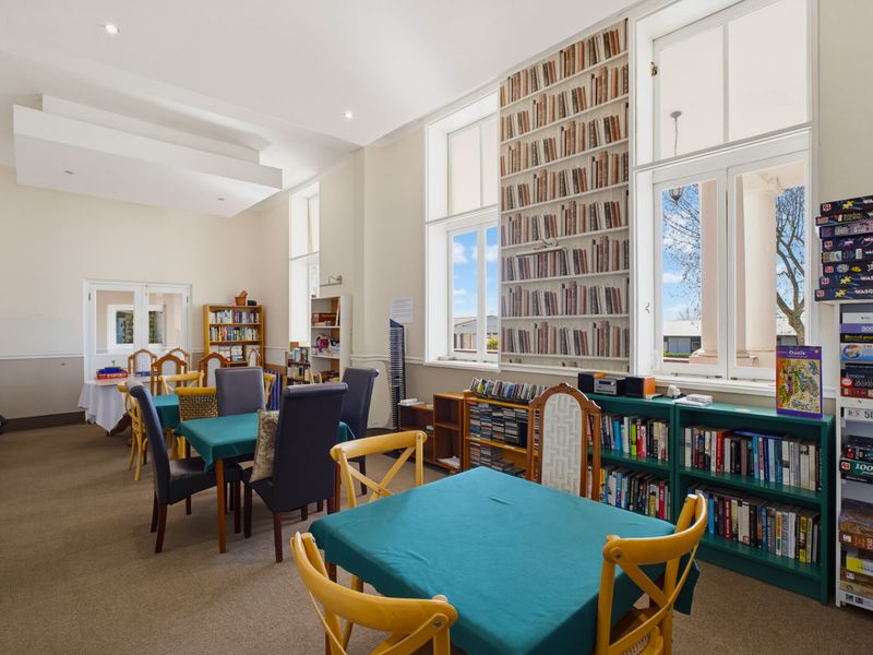 A spacious living area featuring high ceilings, large windows providing natural light, and built-in shelving units.