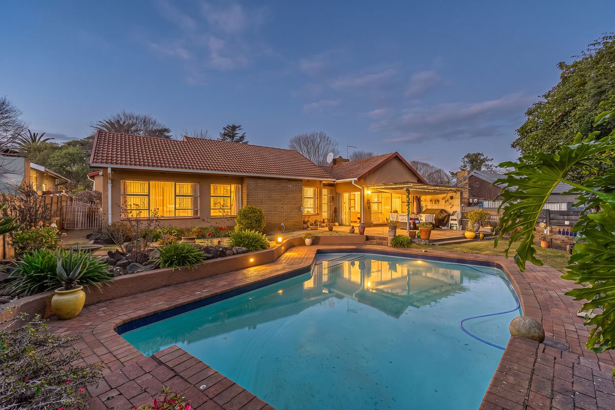 Rear view of the property featuring a swimming pool, brick-paved surround, retaining wall, and a covered patio area.