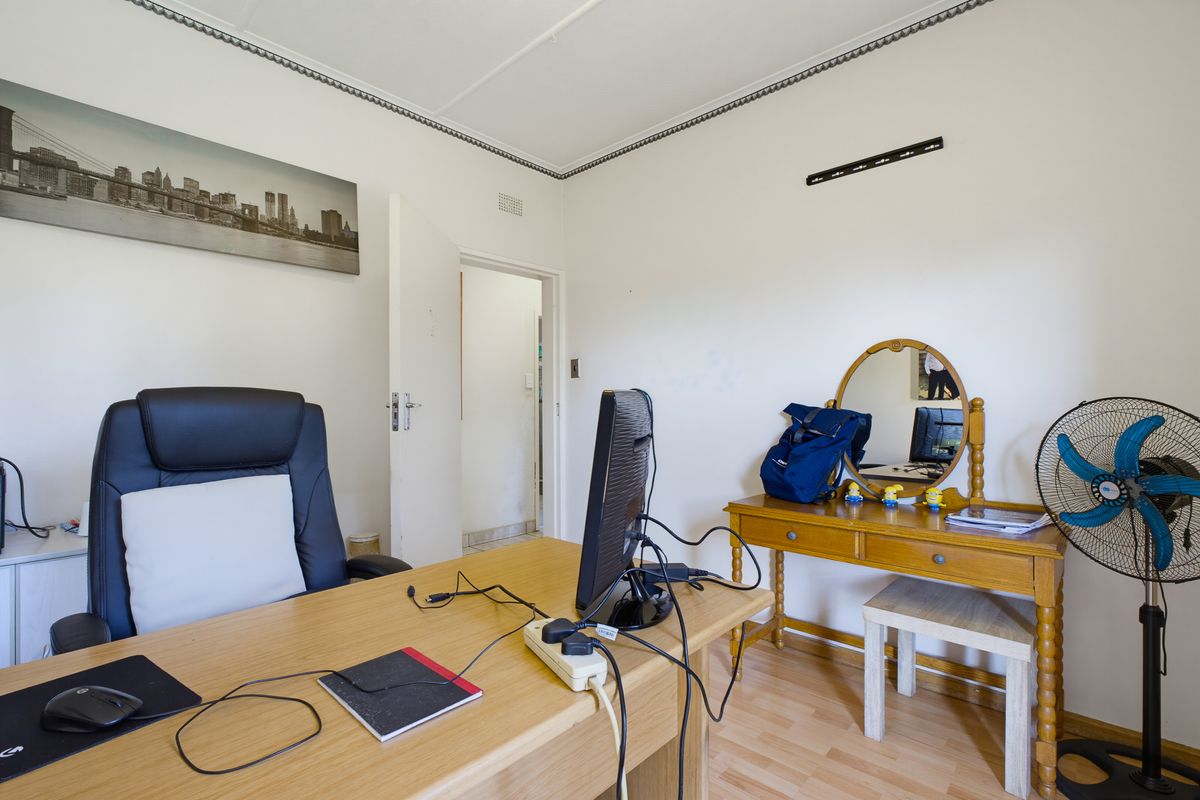 A functional bedroom space featuring laminate flooring and coved ceiling details, currently utilized as a home office.