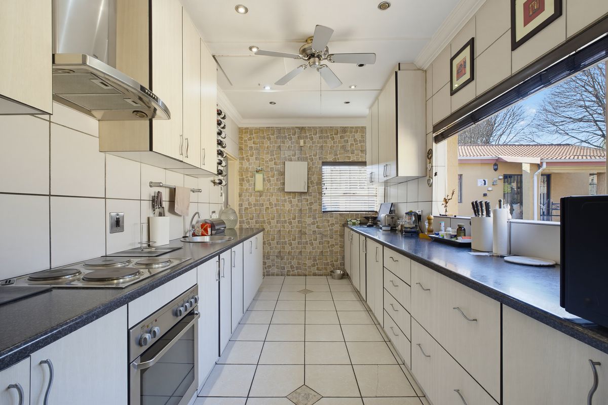 A functional galley-style kitchen featuring light-toned cabinetry, dark countertops, a mosaic feature wall, and integrated cooking appliances with ample storage space.