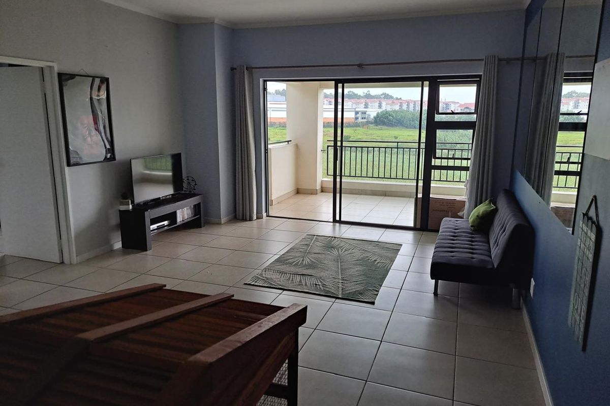 Spacious living room featuring neutral tiled flooring and large sliding glass doors that provide direct access to a private balcony with outdoor views.