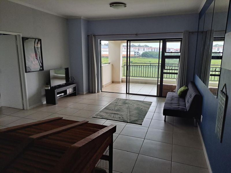 Spacious living room featuring neutral tiled flooring and large sliding glass doors that provide direct access to a private balcony with outdoor views.