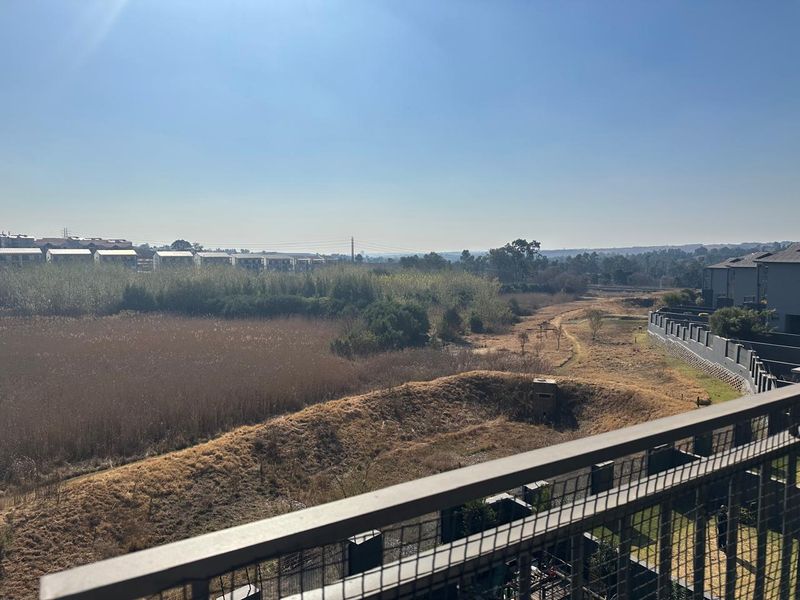 Elevated view from the balcony overlooking a natural landscape, open fields, and surrounding residential development.