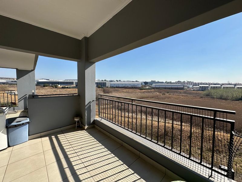 A spacious covered balcony featuring tiled flooring and a metal balustrade, offering an open view of the surrounding landscape.