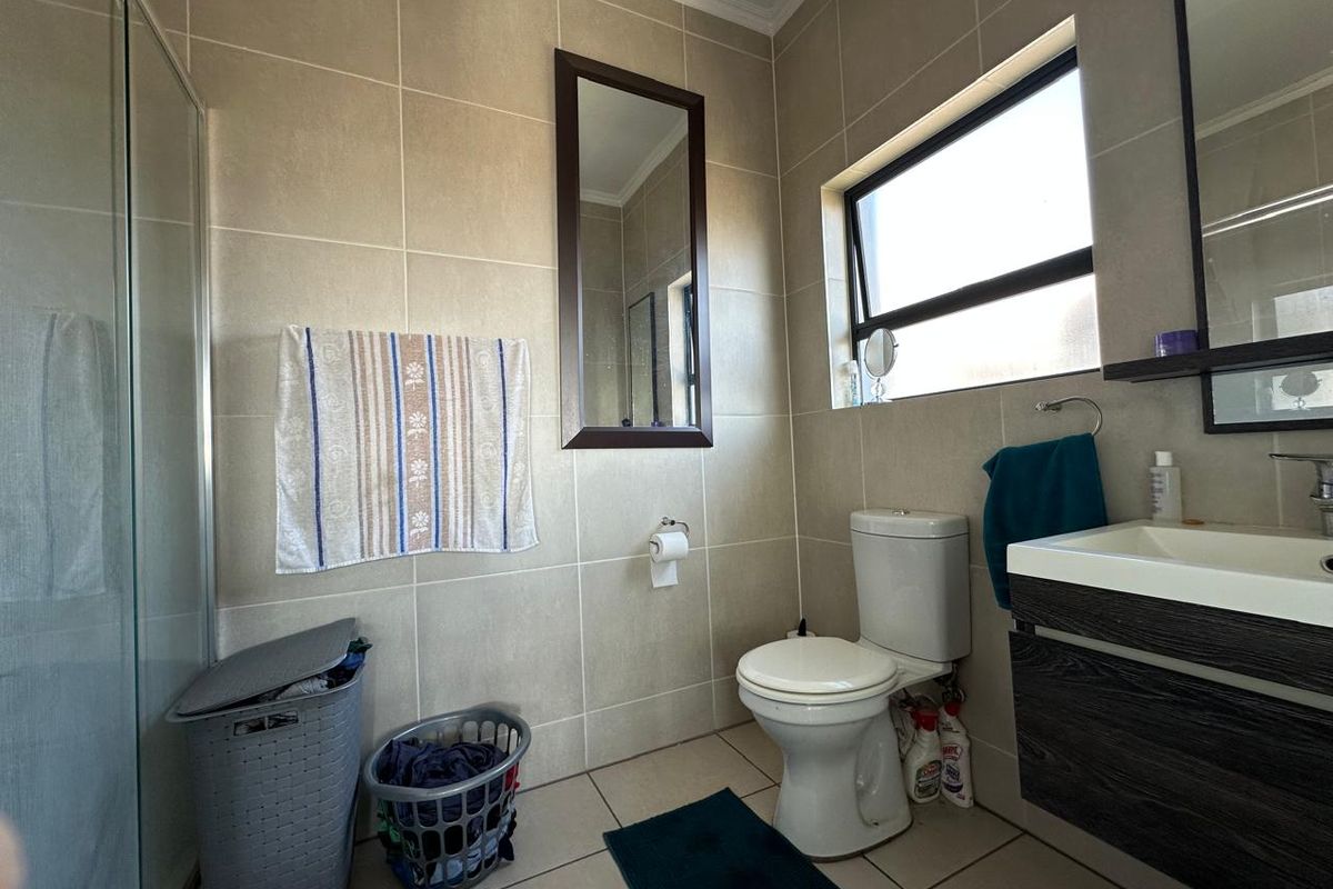 A functional bathroom featuring a shower enclosure, wall-mounted vanity, and neutral wall and floor tiling with a top-hung window for natural light.