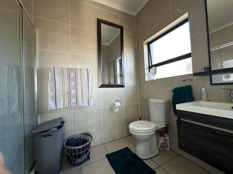 A functional bathroom featuring a shower enclosure, wall-mounted vanity, and neutral wall and floor tiling with a top-hung window for natural light.