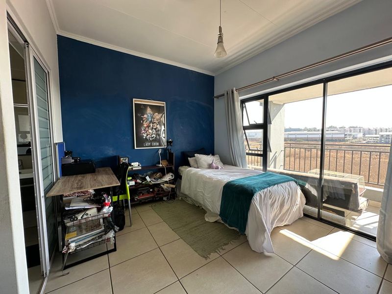 A bedroom featuring tiled flooring, a built-in cupboard, and large sliding glass doors providing access to a balcony with exterior views.