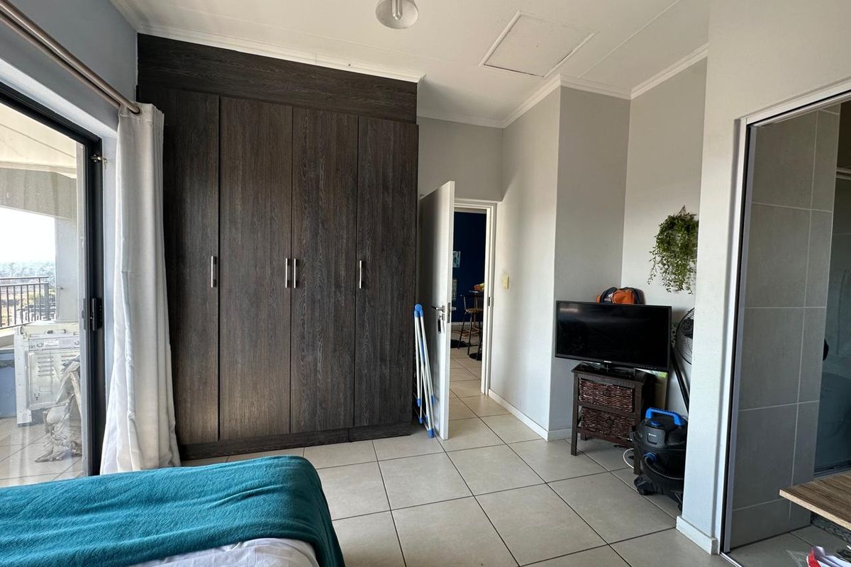 A bedroom featuring dark wood built-in cupboards, neutral tiled flooring, and a sliding glass door providing access to an outdoor balcony area.
