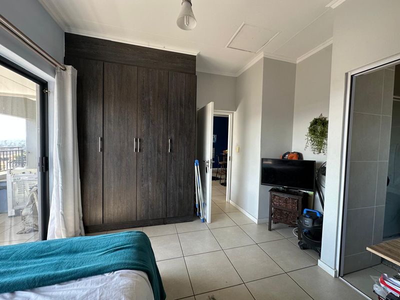 A bedroom featuring dark wood built-in cupboards, neutral tiled flooring, and a sliding glass door providing access to an outdoor balcony area.