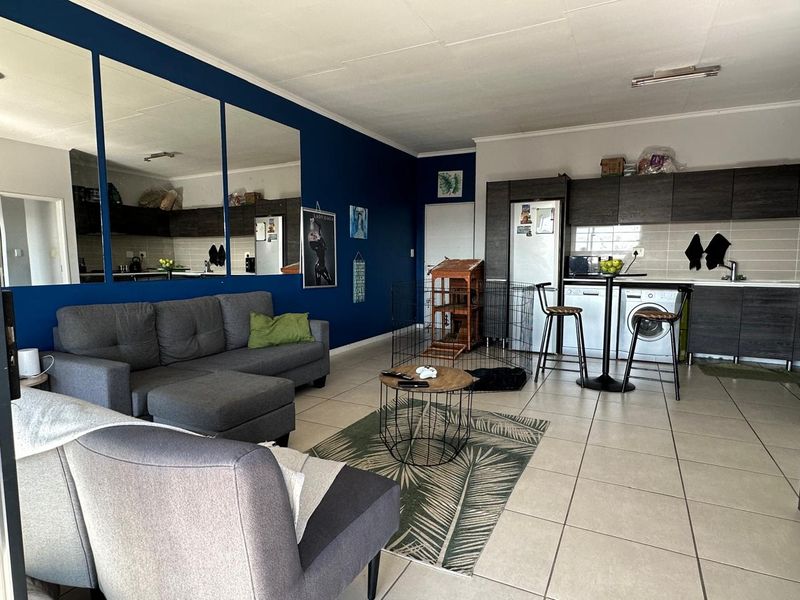 Open-plan living area featuring a modern kitchen with dark cabinetry, tiled flooring, and a bold blue accent wall with large decorative mirrors.