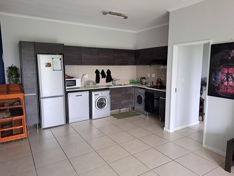 A functional kitchen featuring dark wood cabinetry, tiled backsplash, built-in oven, extractor fan, and neutral ceramic floor tiles.