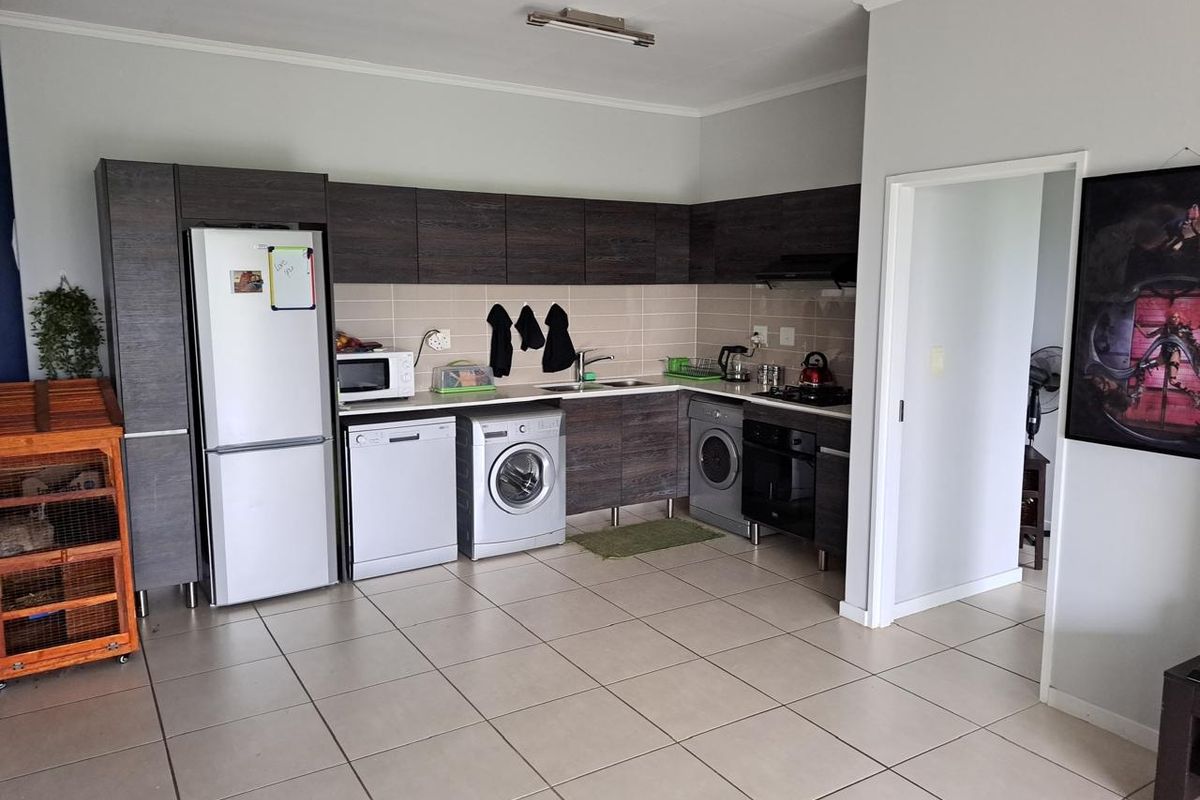 A functional kitchen featuring dark wood cabinetry, tiled backsplash, built-in oven, extractor fan, and neutral ceramic floor tiles.