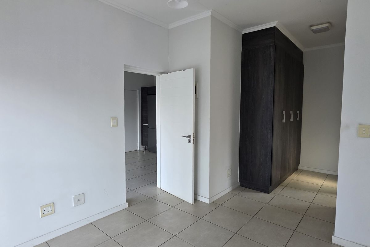 A bright, empty bedroom featuring neutral tiled flooring, white walls, and dark wood built-in cupboards.