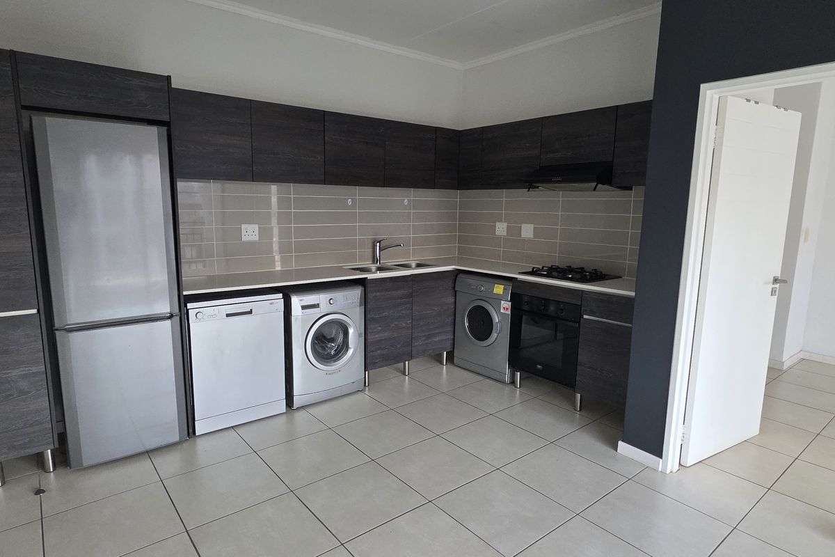 Modern kitchen featuring dark wood-look cabinetry, tiled backsplash, integrated oven and hob, and tiled flooring with adjacent laundry appliance connections.