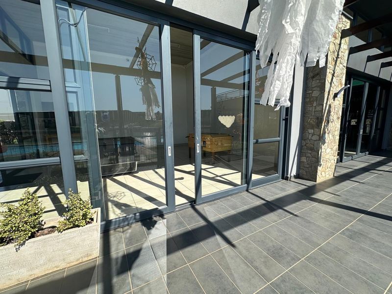 A modern covered patio area featuring dark floor tiles, stone wall accents, and large sliding glass doors leading into the interior space.