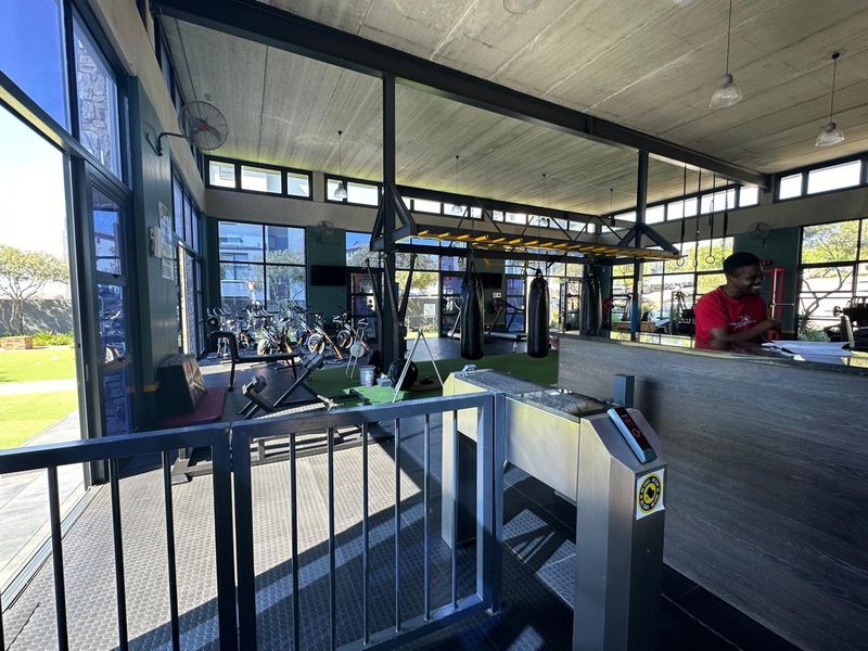 A modern, well-lit gym facility featuring a secure turnstile entrance, reception desk, and expansive windows overlooking the surrounding grounds.