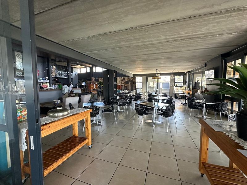 Spacious open-plan commercial dining area featuring tiled flooring, an exposed concrete ceiling, and a built-in bar counter with large sliding glass doors.