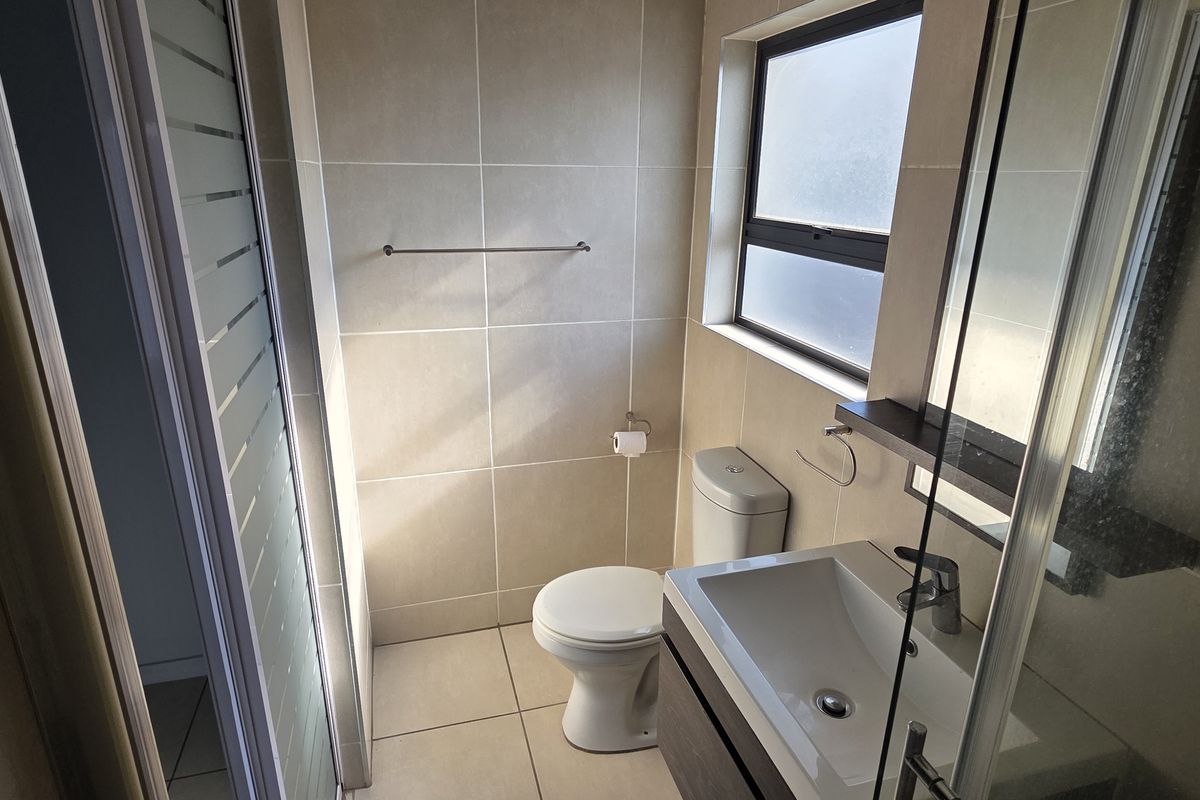 A modern bathroom featuring a shower enclosure, vanity cabinet with basin, and toilet, finished with neutral wall and floor tiles.