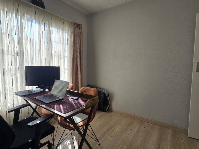 A bedroom featuring laminate flooring and natural light through large windows, currently utilized as a home office space.