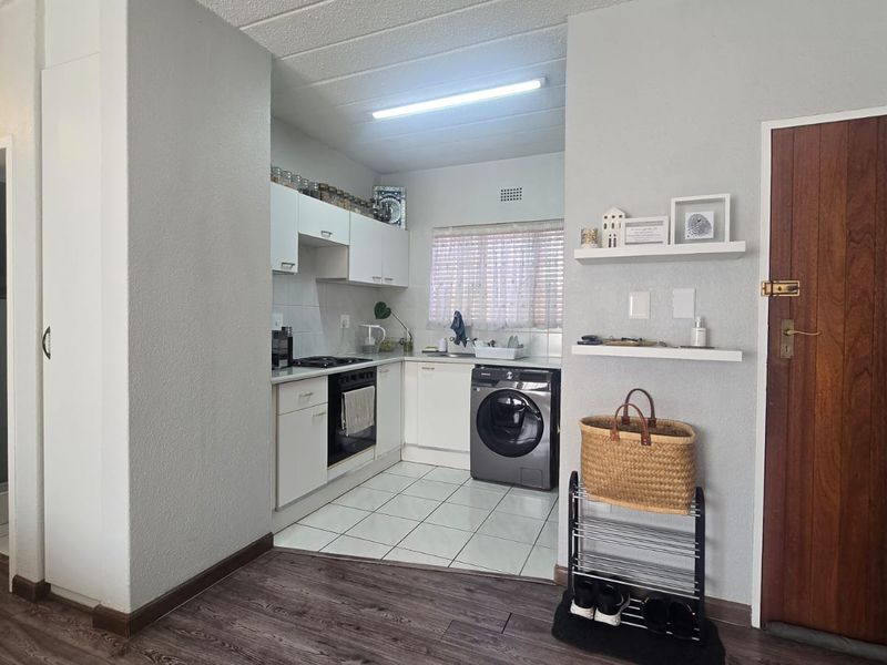 Compact kitchen featuring white cabinetry, built-in oven and hob, tiled flooring, and adjacent laundry area with integrated washing machine.