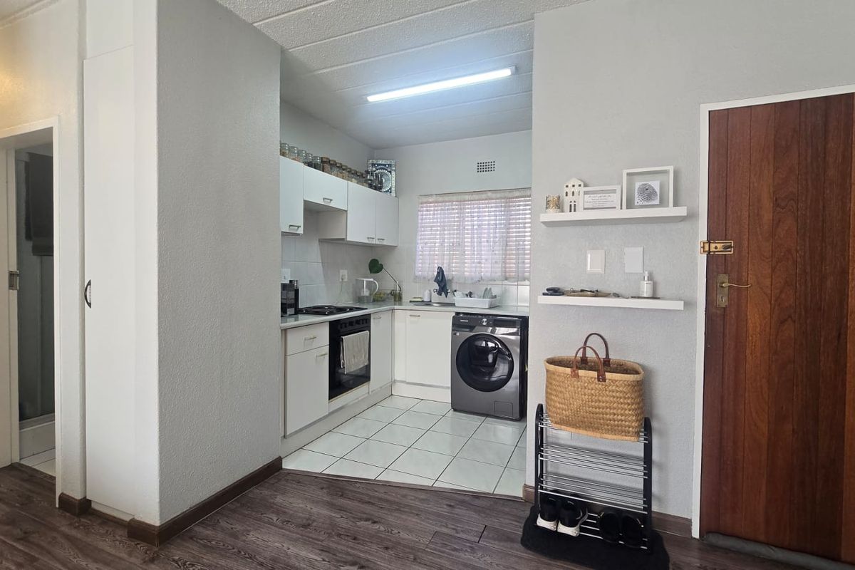 Compact kitchen featuring white cabinetry, built-in oven and hob, tiled flooring, and adjacent laundry area with integrated washing machine.