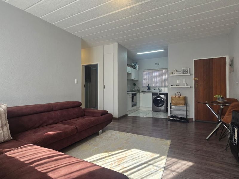 Open-plan living area featuring laminate flooring, a compact kitchen with built-in cabinetry, integrated appliances, and a separate tiled kitchen zone.