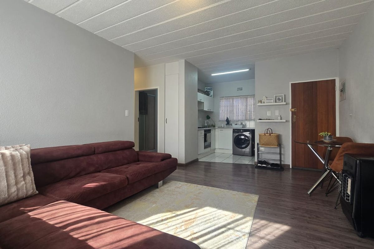Open-plan living area featuring laminate flooring, a compact kitchen with built-in cabinetry, integrated appliances, and a separate tiled kitchen zone.